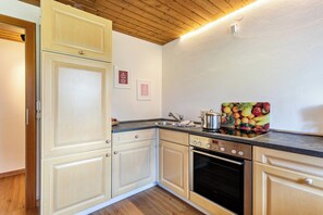 Une cuisine avec des meubles de rangement en bois, un évier en acier inoxydable, un panier de fruits et un four encastré.