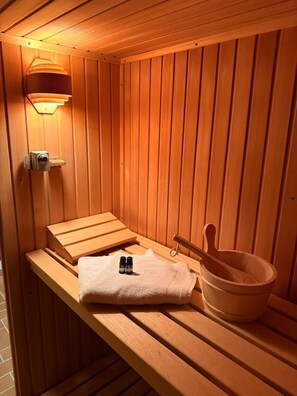 A sauna with wooden benches, a towel, a bucket, and a wall-mounted heater. - Ferienwohnung Chiemgau | Sauna & Bergblick (Unterwössen)