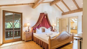A bedroom with a wooden bed, a canopy, a nightstand with a lamp, and a large window with a view of greenery.