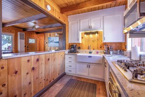 Une cuisine avec des murs en bois, des armoires blanches, un plan de travail en granit et une cuisinière à gaz.