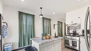 A modern kitchen with a central island, stainless steel appliances, and green curtains. - Lucas Oil Stadium Sanctuary! Hot Tubs! Games! (Indianapolis)