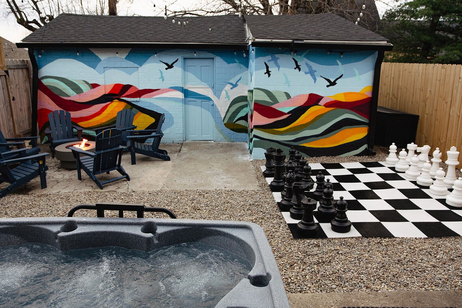 Een achtertuin met een jacuzzi, een vuurkorf, buitenzitplaatsen en een schaakbord.