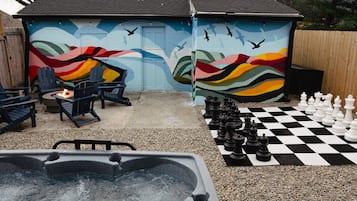 Een achtertuin met een jacuzzi, een vuurkorf, buitenzitplaatsen en een schaakbord.