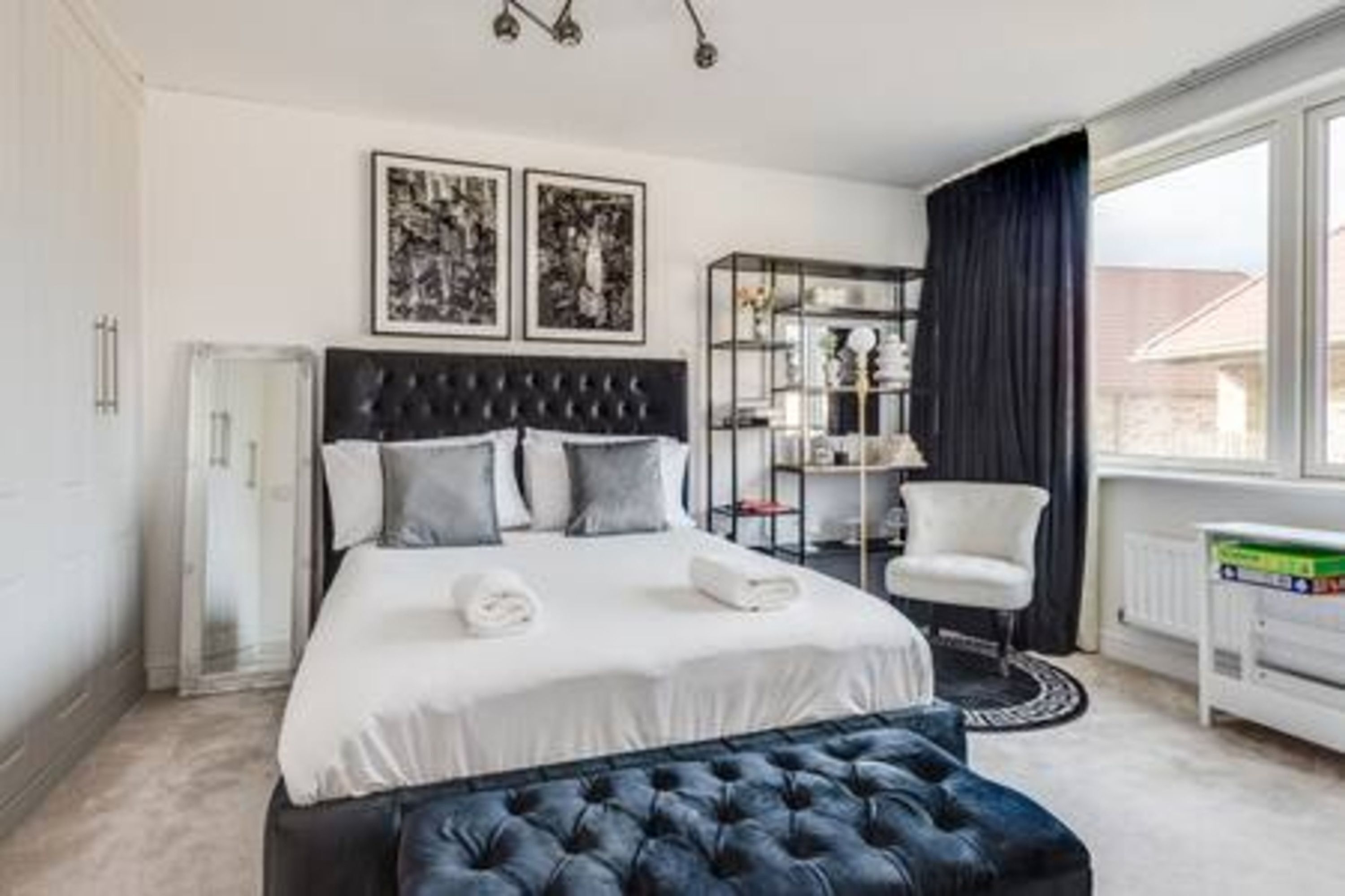 Une chambre à coucher avec un grand lit, une table de chevet, une chaise, une bibliothèque et une fenêtre avec des rideaux.
