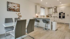 Una cocina moderna con armarios blancos, una isla central con taburetes de bar y un comedor con mesa blanca y sillas grises.