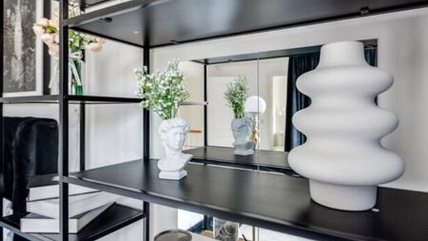 Un interior moderno con estanterías negras, jarrones blancos y una gran escultura blanca.