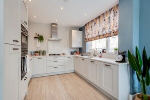 A modern kitchen with white cabinetry, a built-in oven, and a window with a patterned blind.