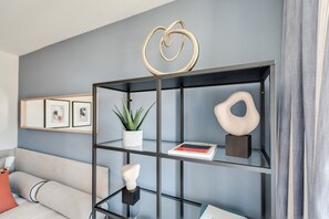 Uma sala de estar moderna com uma estante de vidro, um sofá cinzento e quadros nas paredes.