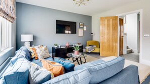 A living room with a blue sofa, a black side table, a yellow chair, and a wooden door. - Stylish 4-br House - Free Parking Nice Garden (Oxford)