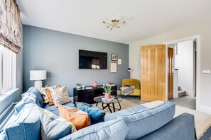 A living room with a blue sofa, a black side table, a yellow chair, and a wooden door. - Stylish 4-br House - Free Parking Nice Garden (Oxford)