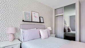 A bedroom with a polka dot wallpaper, a bed with a white and blue polka dot bedspread, two nightstands with lamps, a mirror, and a closet with a sliding door. - Stylish 4-br House - Free Parking Nice Garden (Oxford)
