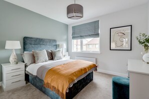 Quarto com cama, mesa de cabeceira, abajur, janela e obra de arte.