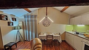 Et kompakt køkken med trægulv, et spisebord med stole, et ur på væggen og en tripodlampe.