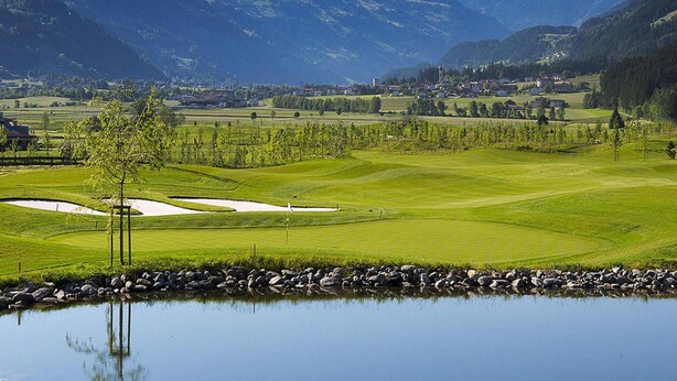 A golf course with a pond, mountains in the background, and a small town. - Apartment in Fugen Near Spieljoch Cable Car (Fuegen)