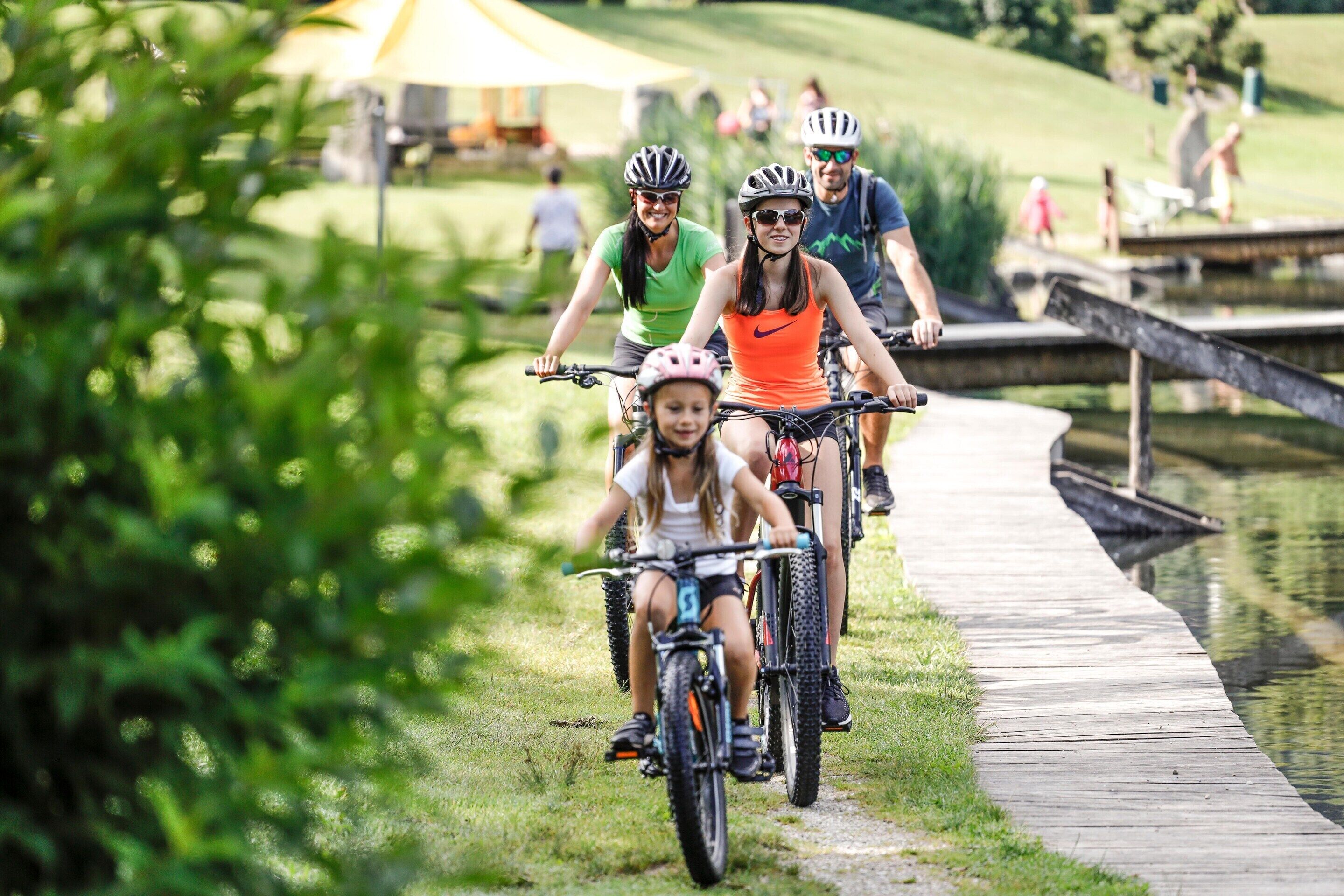 A group of people riding bicycles on a wooden boardwalk beside a body of water.