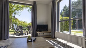 Habitación con televisor sobre un mueble bajo, una mesa con control remoto y vistas al exterior a través de amplios ventanales.