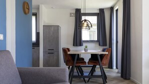 Una sala moderna con un sofá gris, una mesa de comedor con dos sillas y una zona de cocina con un armario gris y un reloj en la pared.