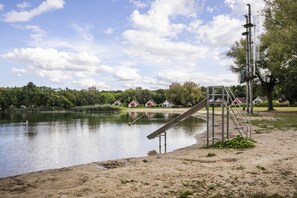 A lakeside park with a playground, a sandy beach, and houses in the background.