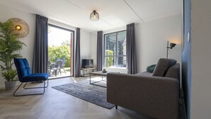 Uma sala de estar moderna com sofá, uma poltrona azul, televisão e uma janela grande.