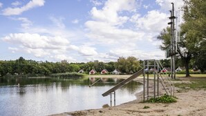 Um parque à beira do lago com um parquinho, uma praia de areia e casas ao fundo.