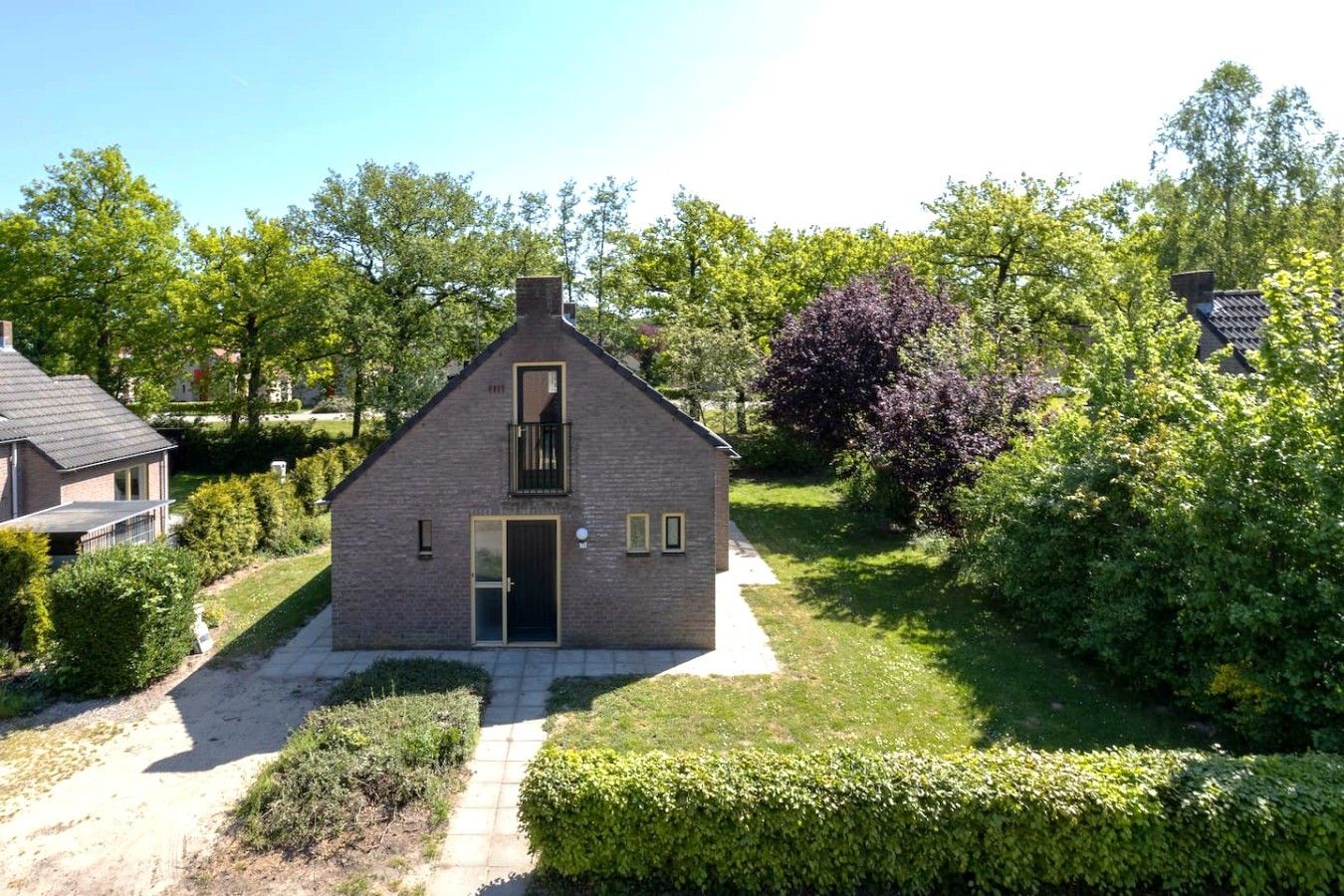 A two-story house with a central entrance, a small balcony, and a garden with various shrubs and trees.
