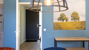 A room with a wooden bench, a door leading to another room, and a wall-mounted picture of trees.