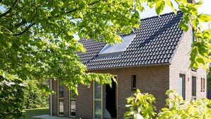 A modern brick house with a sloped roof, large windows, and a visible door.