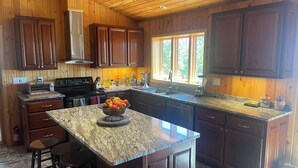 A kitchen with wooden cabinets, granite countertops, a central island with stools, and a window providing natural light. - Lake Vermilion Cabin on a quiet bay with sauna & fire pit for grilling. (Cook)