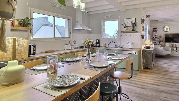 Una cocina moderna con una isla central, iluminación colgante y vista al área de estar.