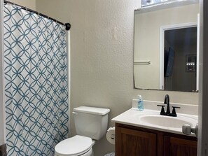 A bathroom with a toilet, a sink, a mirror, and a shower curtain. - Charming 4BR Getaway with 130” Theater, WiFi & AC in San Antonio (San Antonio)