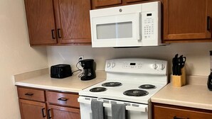 Una cocina con armarios de madera, un microondas blanco, una estufa y una cafetera.