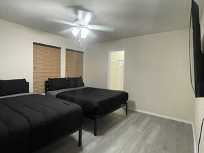 A bedroom with two beds, a ceiling fan, and a door leading to a bathroom. - Charming 4BR Getaway with 130” Theater, WiFi & AC in San Antonio (San Antonio)