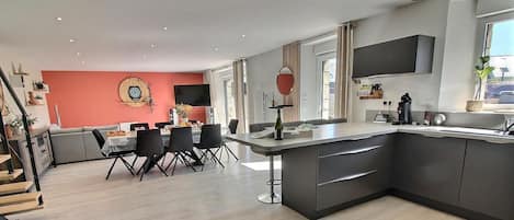 Una cocina moderna con comedor, que cuenta con una isla grande, muebles oscuros y una pared de acento roja.