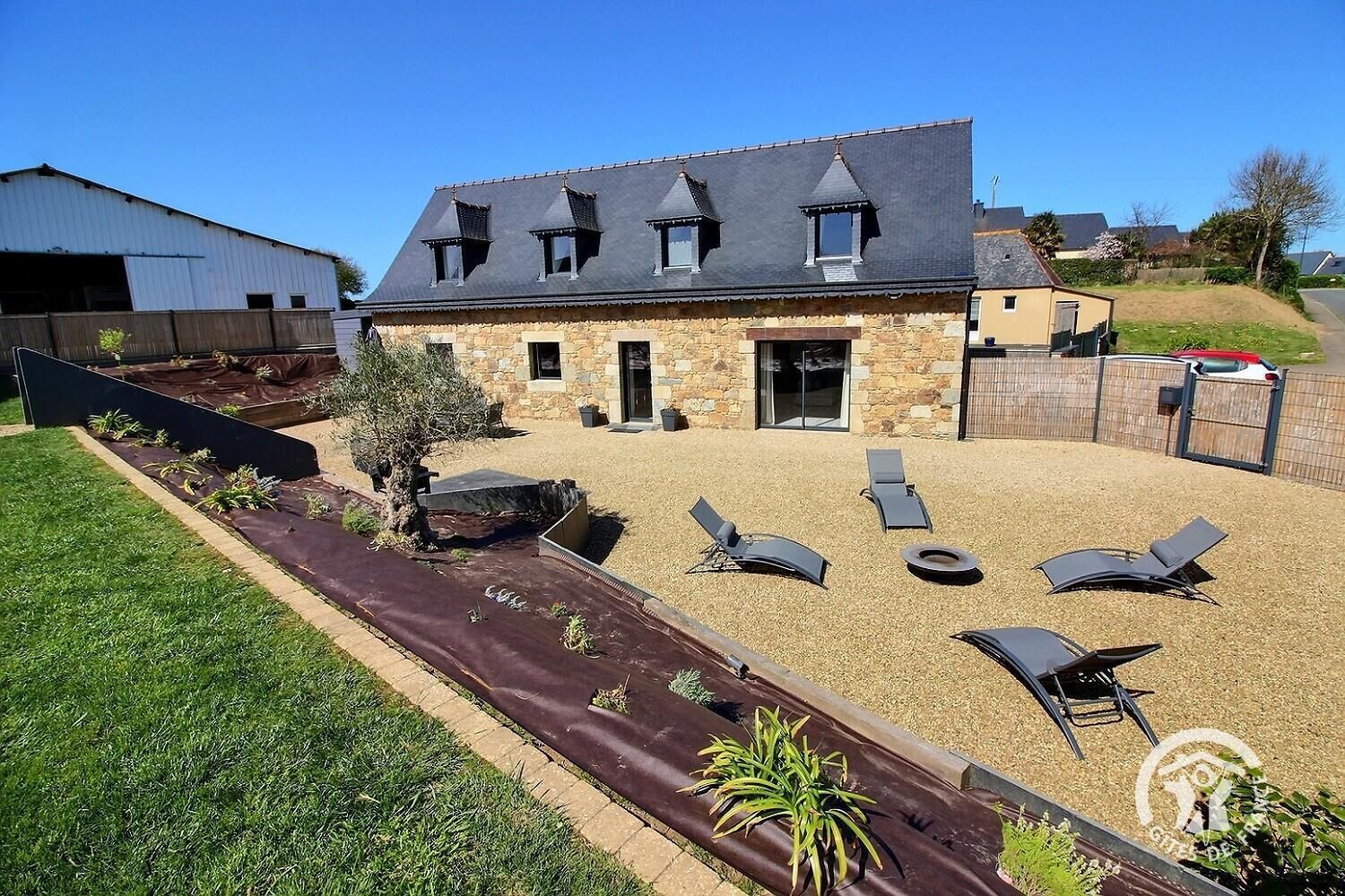 A stone building with a sloped roof and a patio area with lounge chairs and a fire pit.