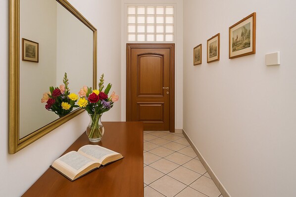 Un couloir avec une porte en bois, un miroir, un vase de fleurs et des tableaux encadrés accrochés au mur.