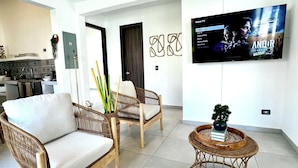 Una sala de estar moderna con muebles de mimbre, un televisor de pantalla plana y una cocina al fondo.