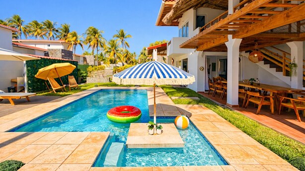 Una piscina con una sandía flotando, una sombrilla a rayas y un balón de playa.
