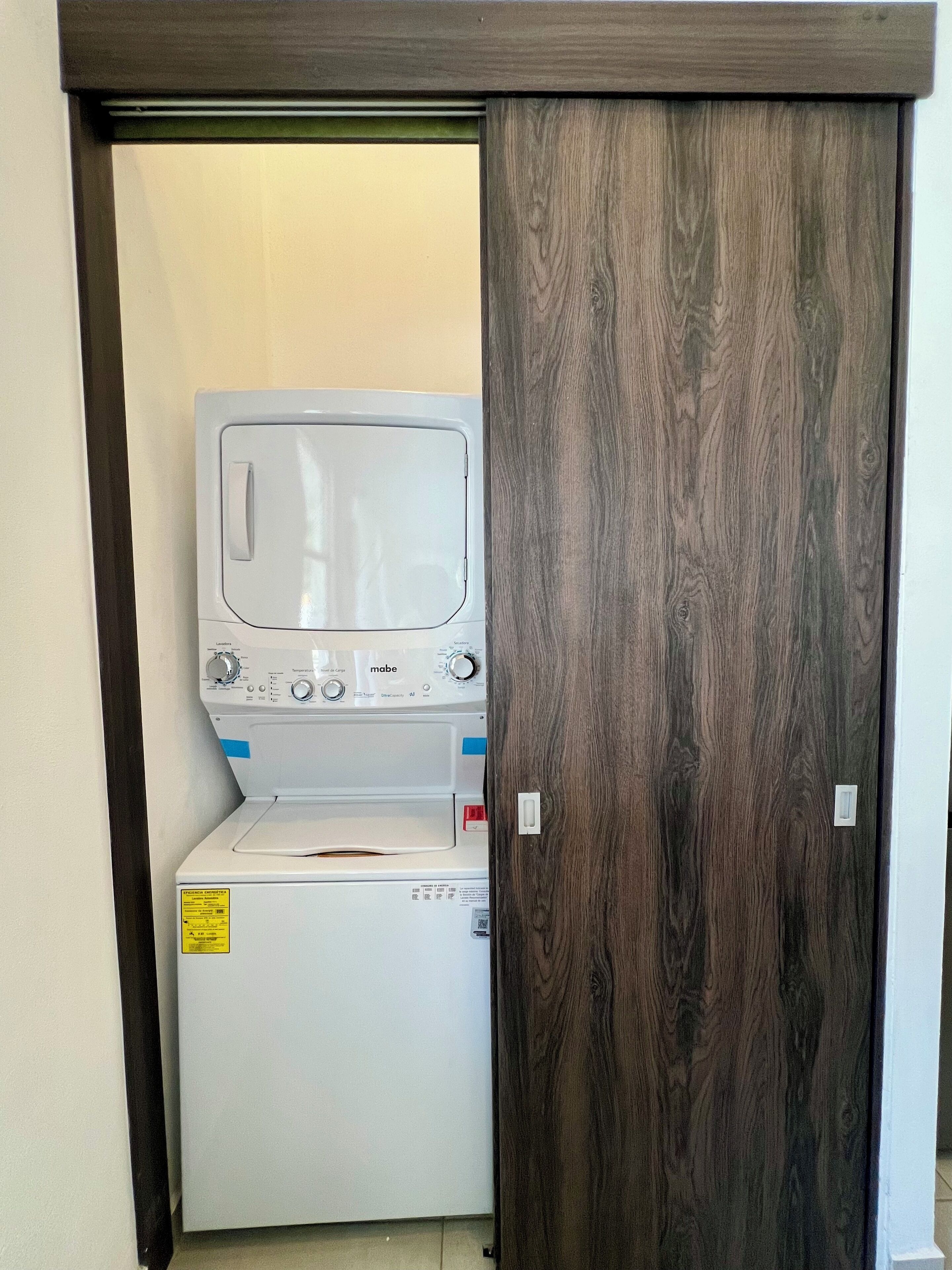 A compact laundry room with a front-loading washer and dryer, a wooden door, and a small window.