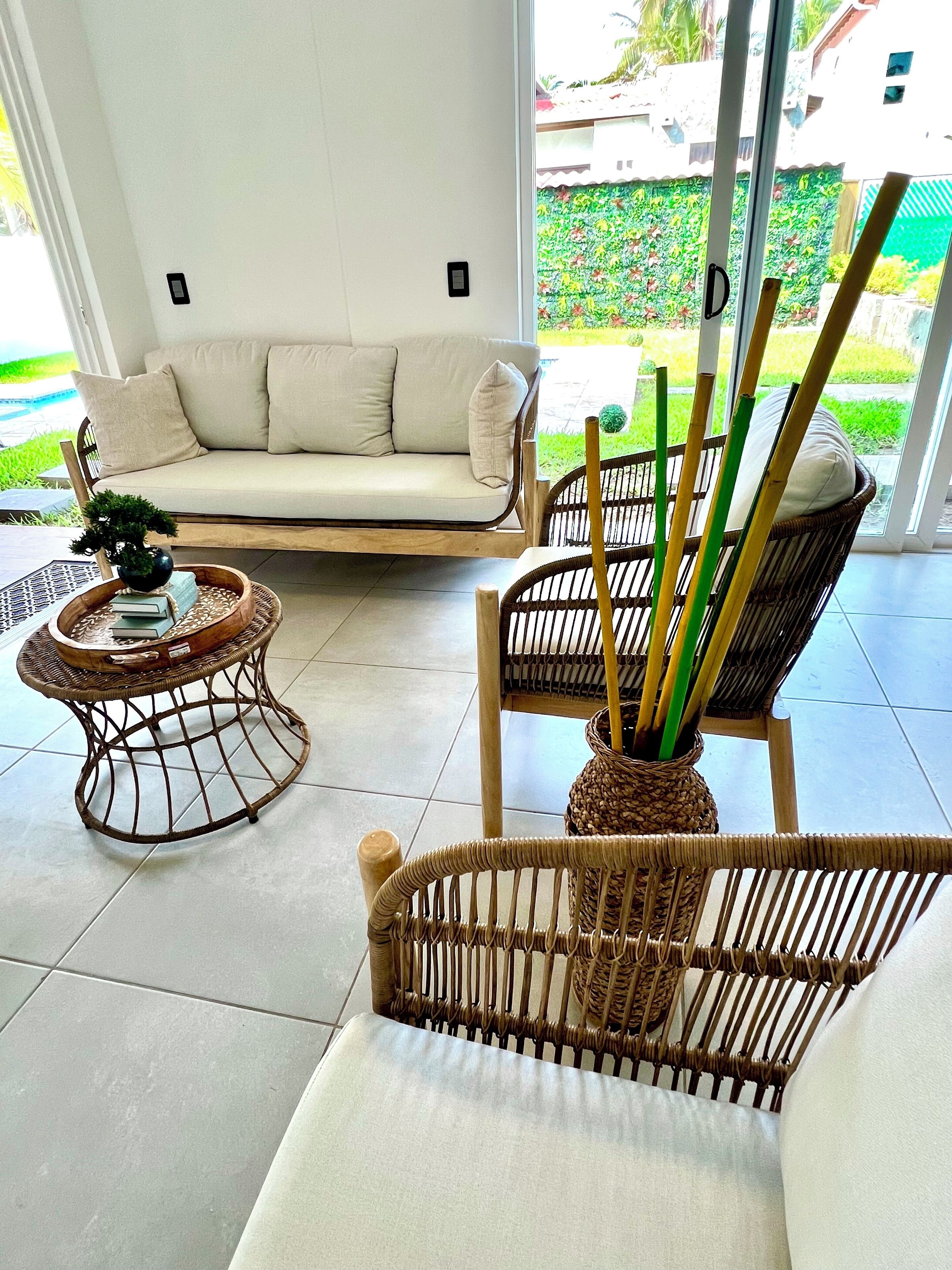 A modern living room with a sofa, wicker chairs, and a small table with a plant.