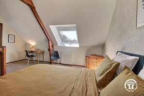 A bedroom with a sloped ceiling, a skylight, a bed with beige bedding, a wooden dresser, and a desk with a chair. - La Ferme rouge, Le Pin (PLUVIGNER)