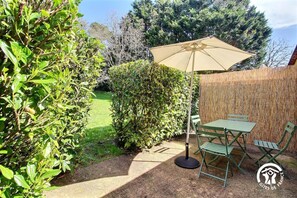 A patio with a table and chairs, a large umbrella, and a bamboo fence. - La Ferme rouge, Le Pin (PLUVIGNER)