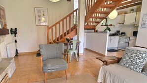 A living room with a sofa, two patterned chairs, a small table, and a staircase leading to a kitchen. - La Ferme rouge, Le Pin (PLUVIGNER)