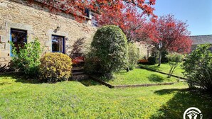 A stone building with a small garden, a red chair, and a well-maintained lawn. - La Ferme rouge, Le Pin (PLUVIGNER)