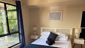 A bedroom with a white bed, a window with curtains, a bedside table with a lamp, and a wall-mounted air conditioner. - Fridays at Three
Wongaling Beach (Wongaling Beach)