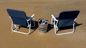 Two beach chairs and a bucket labeled "BEER BUCKET" on a sandy beach with a view of the ocean and distant hills. - Fridays at Three
Wongaling Beach (Wongaling Beach)