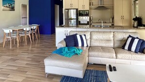 A modern living room with a sofa, a dining table with chairs, a kitchen area with cabinets and appliances, and a ceiling fan. - Fridays at Three
Wongaling Beach (Wongaling Beach)