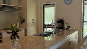 A modern kitchen with a granite countertop, stainless steel sink, and a clock on the wall. - Fridays at Three
Wongaling Beach (Wongaling Beach)