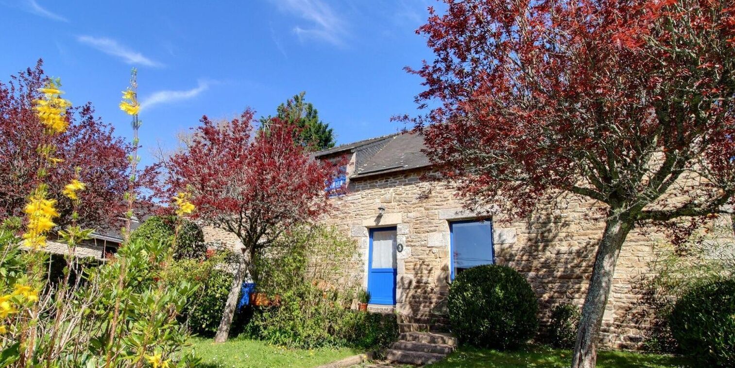 Un bâtiment en pierre avec une porte et des fenêtres bleues, entouré d’arbres aux feuilles d’automne.