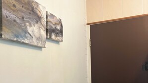 A hallway with a white wall, a black door, and two abstract paintings.