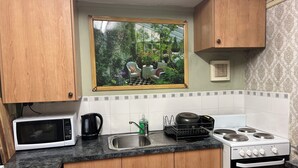 A kitchen with wooden cabinets, a microwave, a kettle, a sink, and a stove.